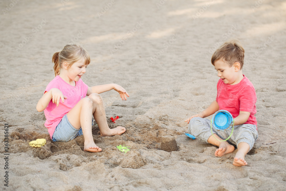 Two Caucasian children sitting in sandbox playing with beach toys. Little girl and boy friends having fun together on playground. Summer outdoors activity for kids. Leisure time lifestyle childhood. Two Caucasian children sitting in sandbox playing with beach toys. Little girl and boy friends having fun together on playground. Summer outdoors activity for kids. Leisure time lifestyle childhood.