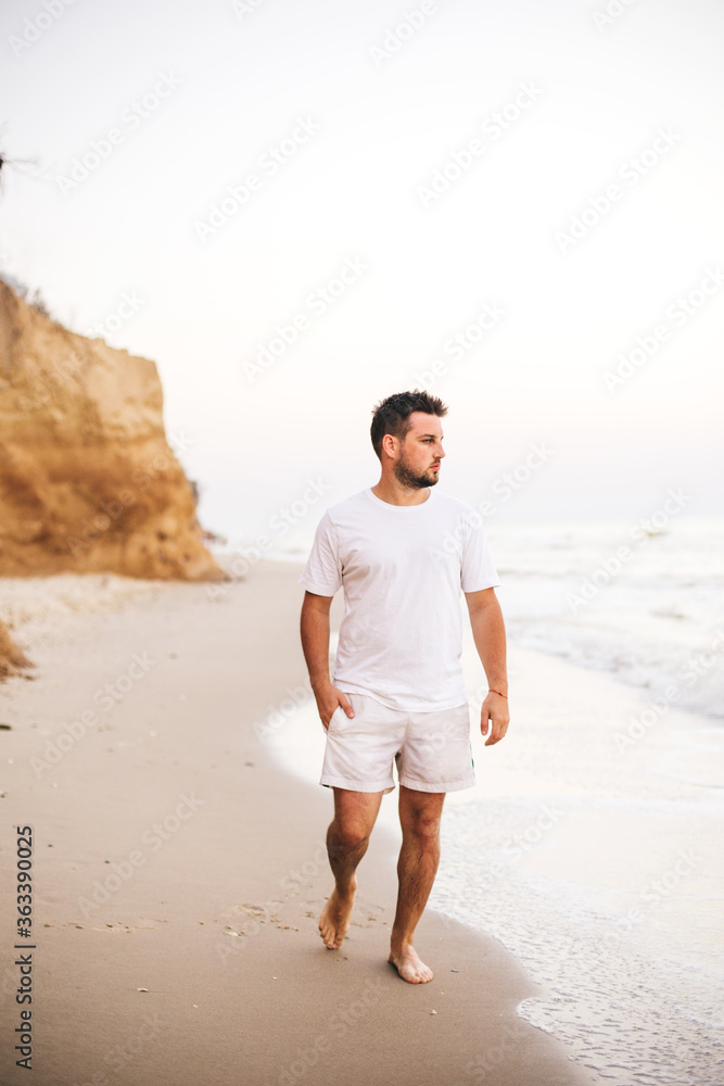 Young man in white t-shirt walking on beach