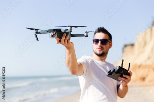 Young man holding drone before flight near ocean or sea. Pretty guy prepare to pilot outdoor