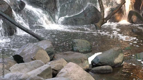 Stationary shot of water cascading down a rocky waterfall into the river below with boulders in foreground and white bubbles forming on the surface of the water. photo