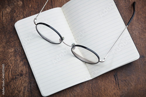 black glasses spread on blank notepad with lines for notes on wooden desk