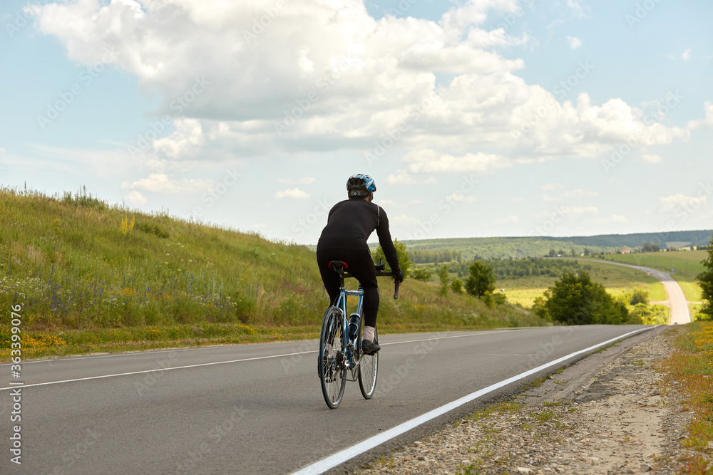 A professional cyclist rides on an empty highway going down a hill, beautiful nature on the horizon on a Sunny day.