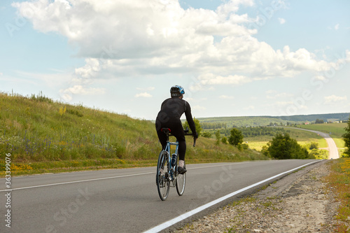 Fototapeta Naklejka Na Ścianę i Meble -  A professional cyclist rides on an empty highway going down a hill, beautiful nature on the horizon on a Sunny day.