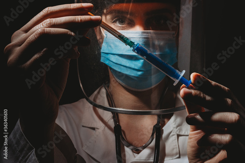 Female doctor with mask and shield holding vaccine in hands on black background