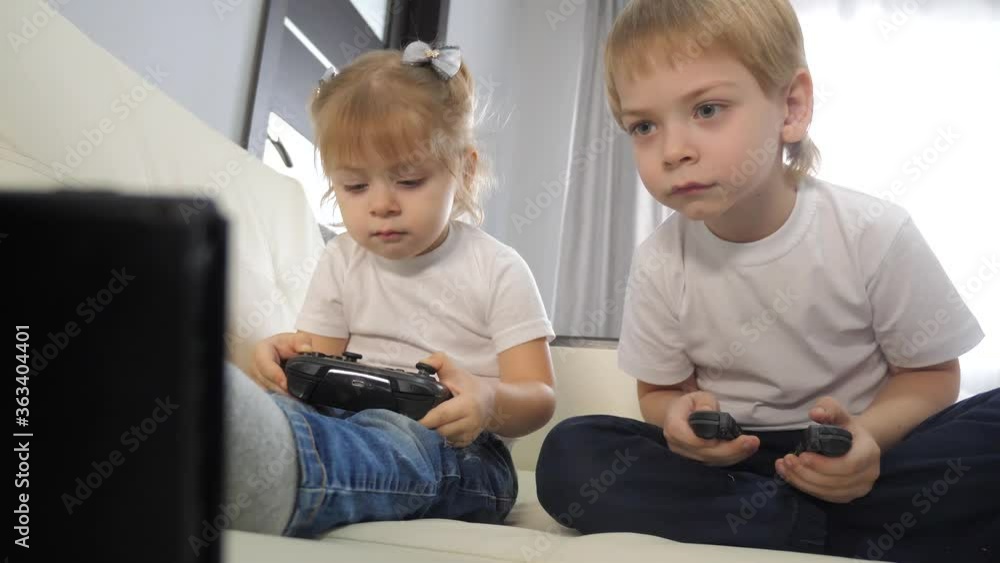 children play lifestyle console in gamepads teamwork. kids a boy and a girl are playing a portable set-top box in a TV controller. happy family little boy and girl have fun online games children play lifestyle console in gamepads teamwork. kids a boy and a girl are playing a portable set-top box in a TV controller. happy family little boy and girl have fun online games