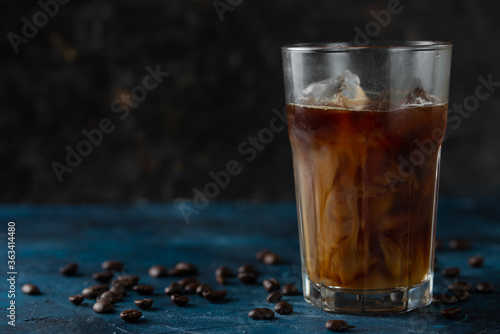 Ice cold coffee with ice cubes and coffee grains on a blue background. Cold summer drink with pipes