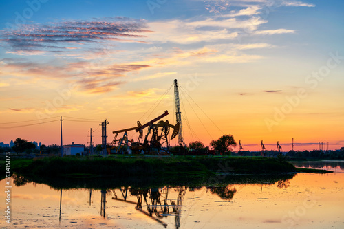 Oil Pumping Unit by the lake in the sunset.