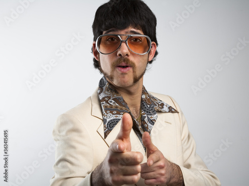 Portrait of a retro man in a 1970s leisure suit and sunglasses pointing to the camera