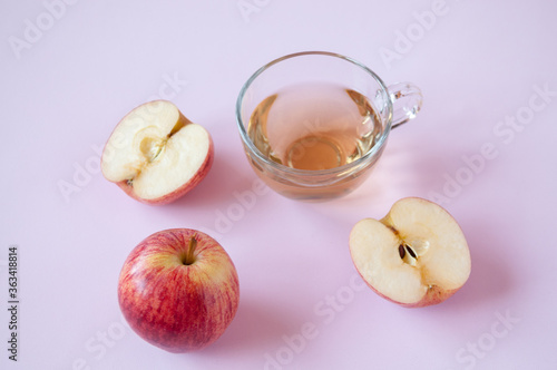 A whole and cut red Apple and a transparent Cup of Apple juice on a pink background