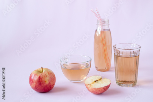 Glassware with Apple juice  whole and half of a red Apple on a pink background
