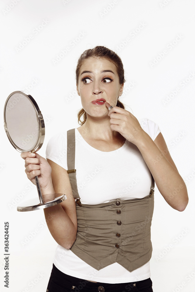 Woman holding hand mirror while applying lipstick Woman holding hand mirror while applying lipstick