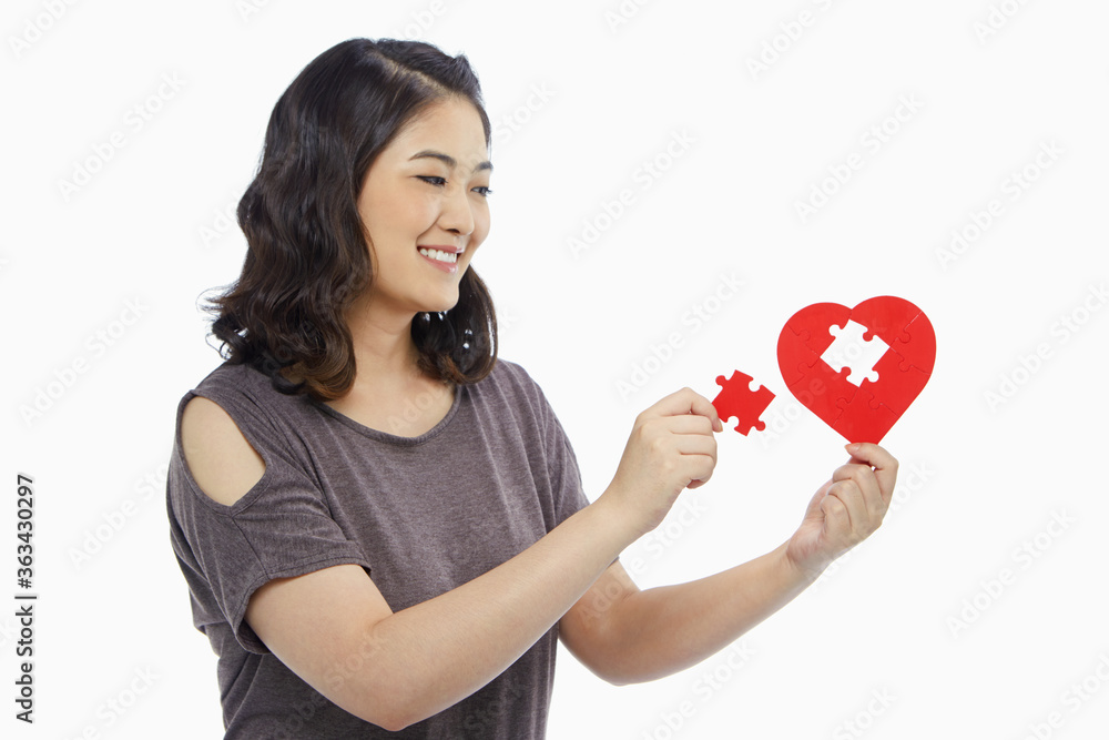 Woman holding a puzzle piece from a heart shape Woman holding a puzzle piece from a heart shape