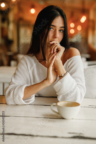 Thoughtful mature woman sitting in cafeteria holding coffee mug while looking away. Brunette woman drinking tea while thinking. Relaxing and thinking while drinking coffee. © Yevhenii