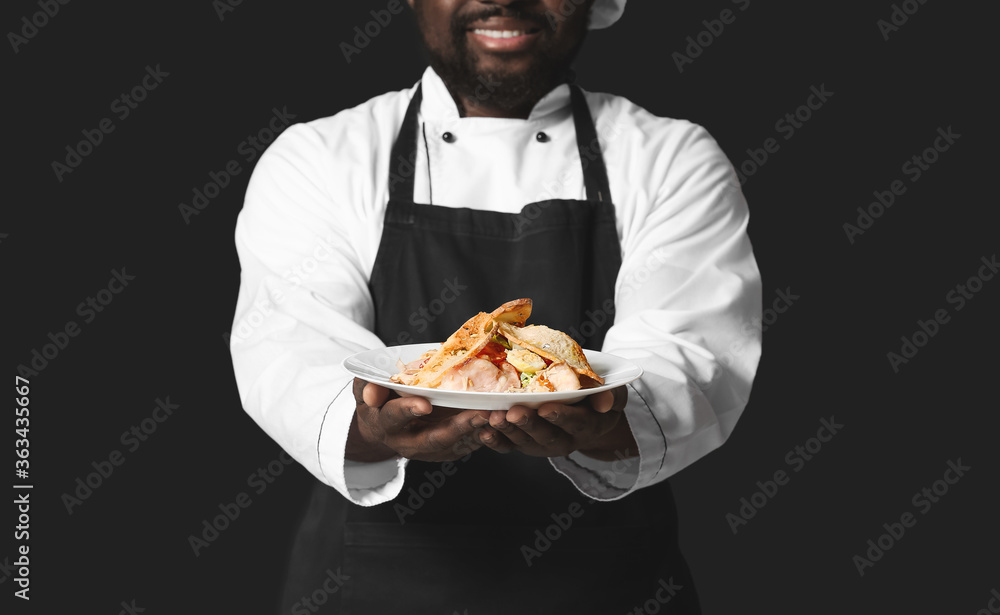 Male African-American chef with tasty dish on dark background Male African-American chef with tasty dish on dark background