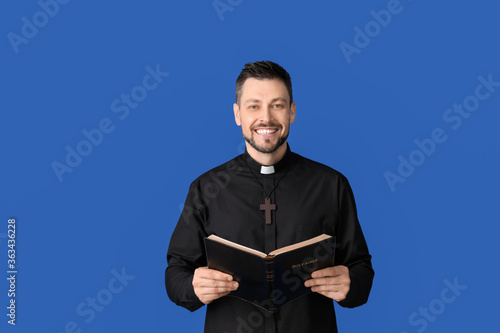 Handsome priest with Bible on color background