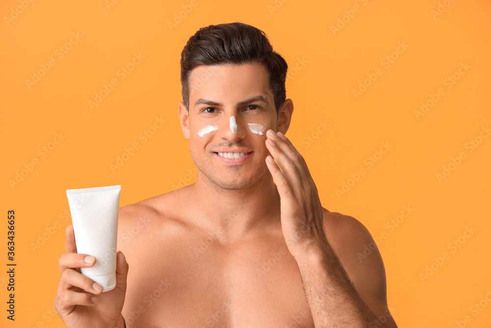 Young man applying sunscreen cream against color background Young man applying sunscreen cream against color background