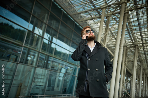 Urban business man in sunglasses talking smart phone traveling walking outside airport. Casual young businessman wearing suit jacket. Handsome male model in 20s, Manager, City Hall, cell.