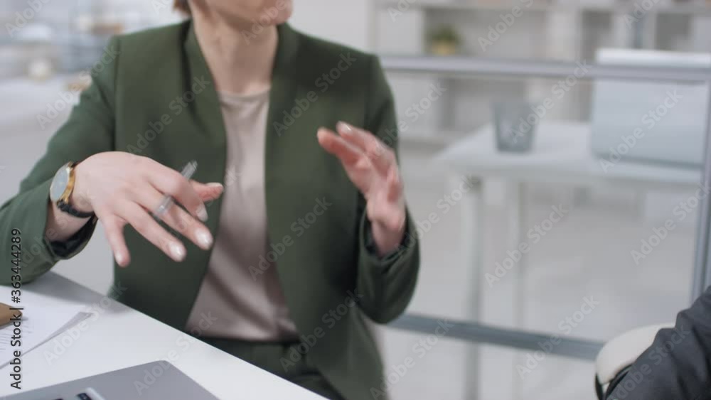 Young businesswoman and unrecognizable businessman sitting together at office desk making business agreement and shaking hands Young businesswoman and unrecognizable businessman sitting together at office desk making business agreement and shaking hands