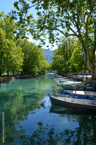 Alpine town Annecy in Upper Savoy, France, colorful boats on river Thiou, trees on both sides of the riverbanks, a sunny day in summer