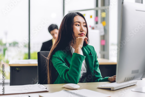 Beautiful confident asian businesswoman looking at document report while sitting on office desk.Young creative coworkers business people working on desktop computer and typing on keyboard at office