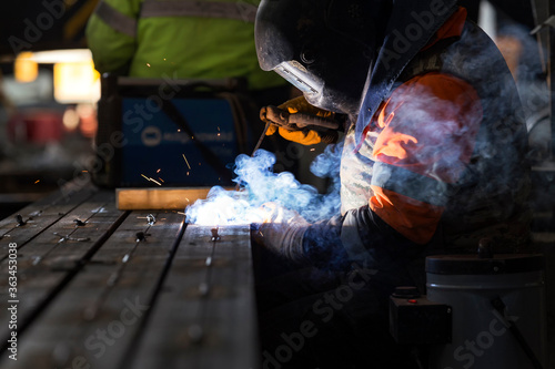 The welder is welding with shielded metal arc welding (SMAW). It is also known as manual metal arc welding (MMAW) or stick welding. Electric current is used to strike an arc.
