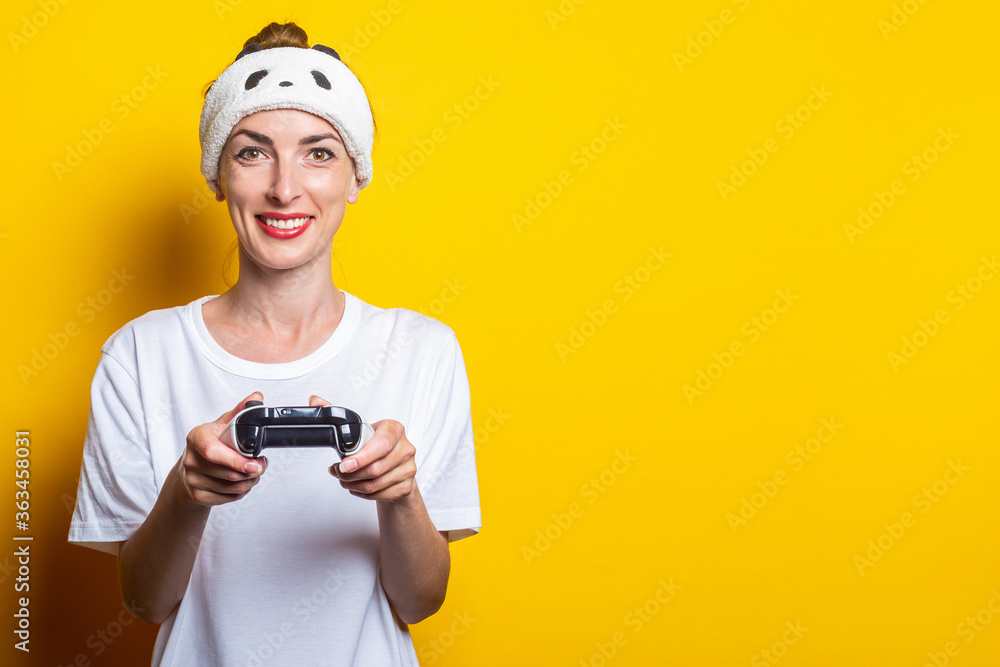 Young smiling woman playing a virtual game with a joystick in their hands on a yellow background. Young smiling woman playing a virtual game with a joystick in their hands on a yellow background.