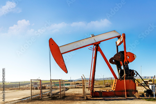 Close up view of the pumpjack in the oil well with cloudy and blue sky. pumpjacks worked by rod lines running horizontally above the ground to a wheel on a rotating eccentric in a mechanism.