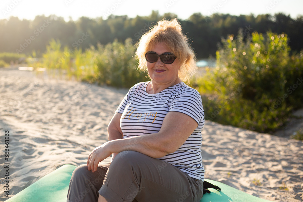 happy senior beautiful woman sitting on a sand in summer beach