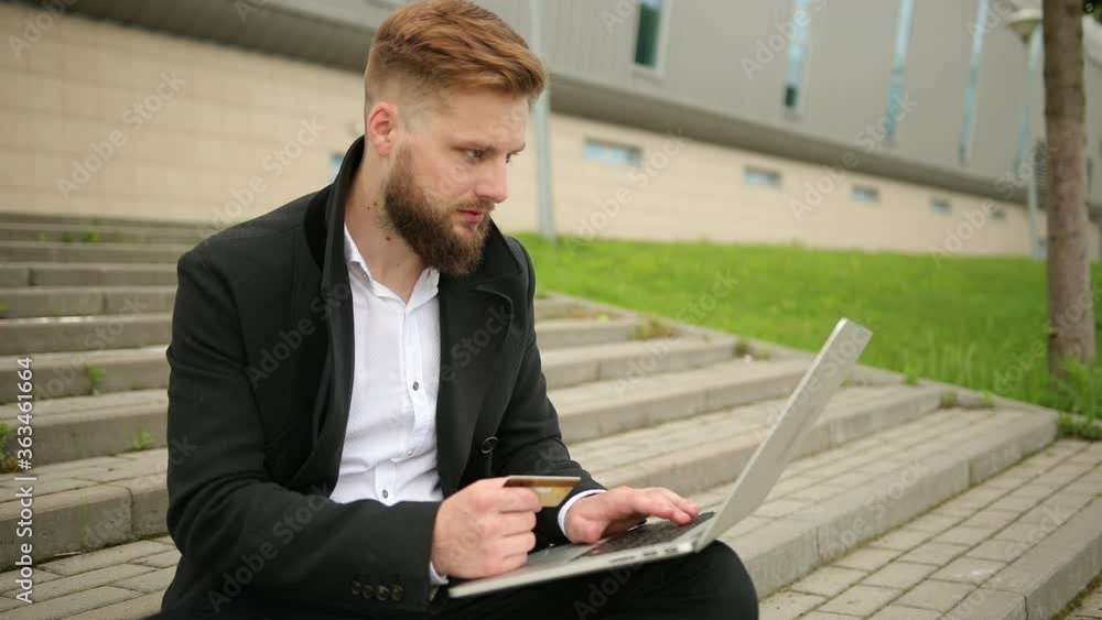 Closeup young man hands holding credit card and using computer laptop for online shopping or reporting lost card, fraudulent transaction, isolated city outside background. New generation technology. Closeup young man hands holding credit card and using computer laptop for online shopping or reporting lost card, fraudulent transaction, isolated city outside background. New generation technology.