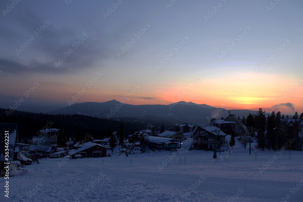 view over dark mountain chain, village, forest and ski trail on the foreground