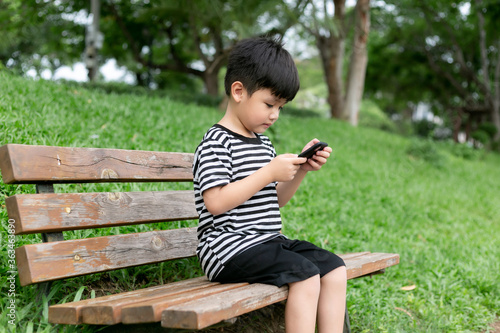 Cute little boy sitting on a park bench and playing with mobile phone