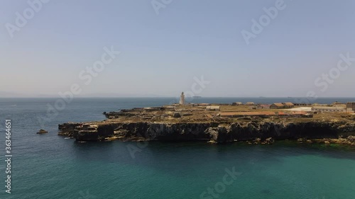 Aerial view of the fortress island of Punta Tarifa in southern Spain. The drone is flying towards the island. In the background is the Strait of Gibraltar. Ships sail towards the Atlantic.