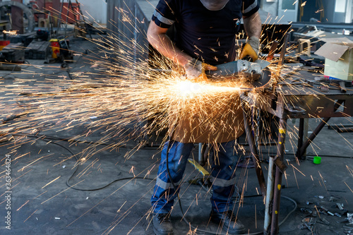 The metal worker is grinding to a steel material with a hand grinding machine in the steel factory.