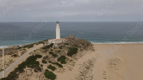 The Trafalgar lighthouse from the air. The drone flies a quarter circle. It is a cloudy summer day. In the background the Atlantic Ocean.