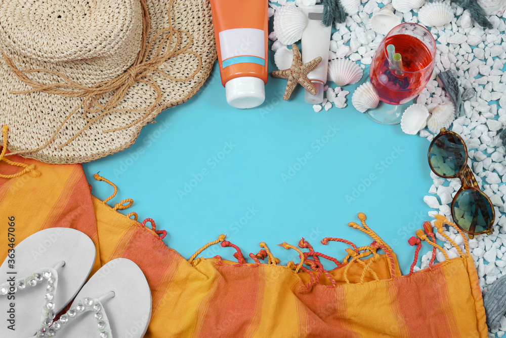 Beach summer composition with straw hat,  shells, pebbles, sponges, sunscreens, sunglasses, cocktail glass, flip-flops and coloured towell on light  blue plain background. Space for text. 