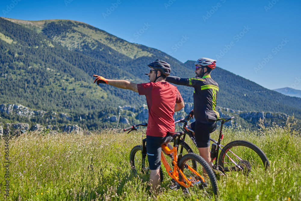 Fototapeta premium two men on mountain bikes in the middle of the mountain pointing to a point