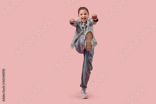 Full-length girl in fashionable jeans clothes and sneakers. Pink background.
