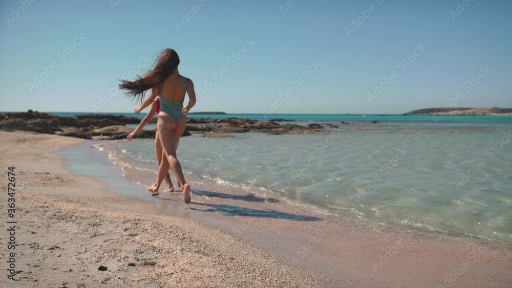 Two attractive young girls in swimsuit running on the beach in slow motion on sea shore. Pretty girlfriends having fun on sunny summer day. Concept of travel, vacation, enjoying life, youth. Two attractive young girls in swimsuit running on the beach in slow motion on sea shore. Pretty girlfriends having fun on sunny summer day. Concept of travel, vacation, enjoying life, youth.