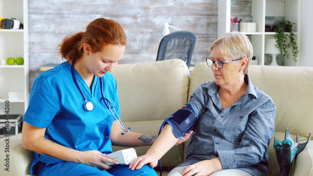 Obraz premium Female doctor taking blood pressure of senior woman in nursing home sitting on sofa