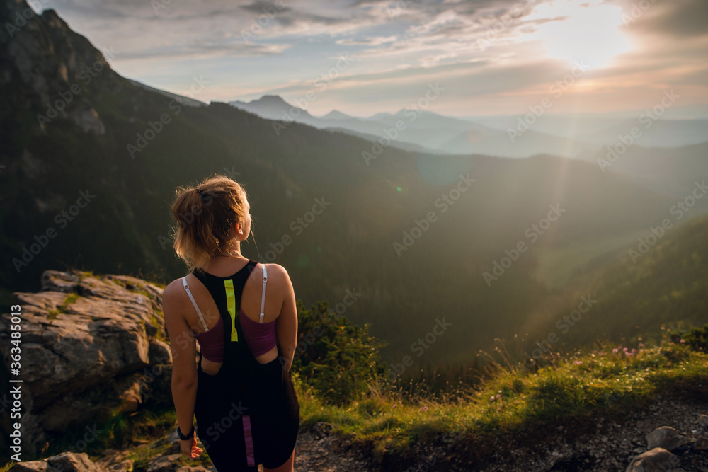 Naklejka premium Rear view shot of young fit woman in sportswear looking on the scenic view of mountains on sunset. Rysy mountains, Tatras. Poland, Slovakia
