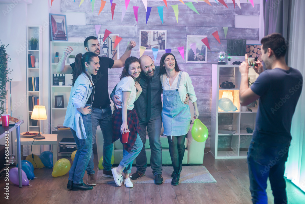 Obraz premium Man taking photos of friends laughing at a party in an apartment.