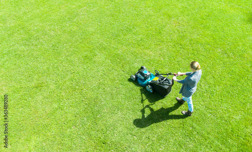 Beautiful girl cuts the lawn. Mowing lawns. Aerial view beautiful woman lawn mower on green grass. Mower grass equipment. Mowing gardener care work tool. Aerial lawn mowing
