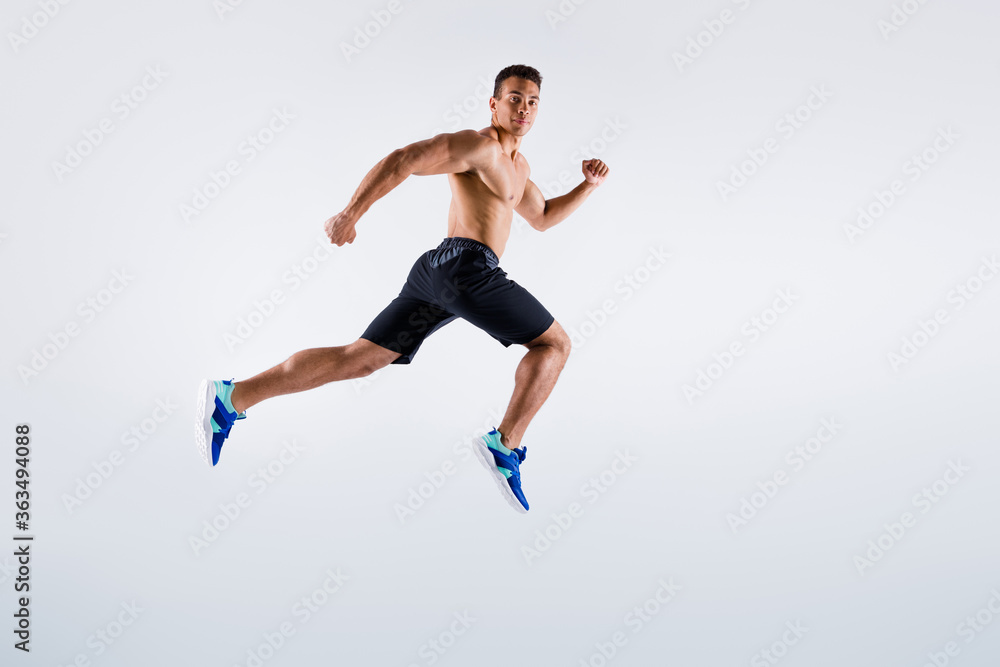 Full length profile photo of handsome sportsman dark skin guy naked chest jumping high up running fast sprint workout exercise wear shorts sneakers isolated white color background