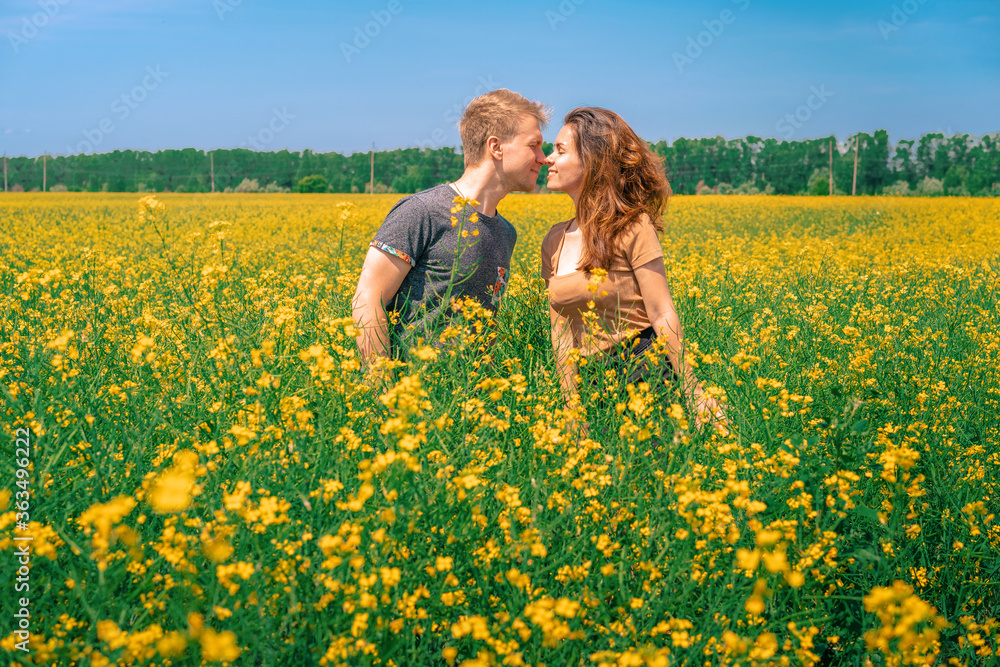 Fototapeta premium A young man and woman embrace in a Sunny yellow rapeseed field, the concept of travel and freedom, a bright banner for summer