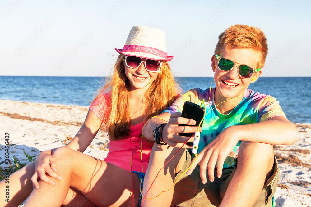 Teenagers (boy and girl) using smart phone and listening music on the beach.