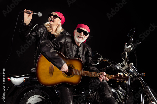Photo of aged bikers man lady duet couple sit chopper moto rock bike festival meeting play sing guitar songs remember youth wear rocker leather jacket pants isolated black color background