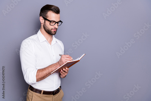 Photo portrait of concentrated intelligent guy in formal wear holding opened notepad using it to write strategy plan isolated over grey background