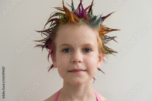 A child looks at the camera, a close-up portrait. The hair of a girl or boy is colored in different colors. The festival of colors, summer holiday