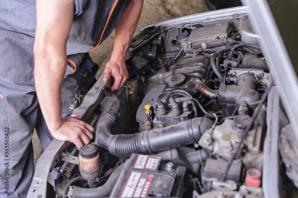 Mechanic in working overalls looking at a car engine.