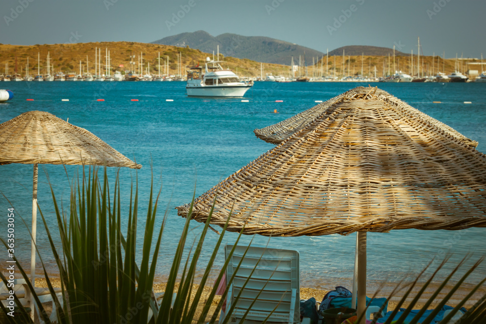 Fototapeta premium Thatched sun umbrellas, beach umbrellas on the sea background with blurred yachts
